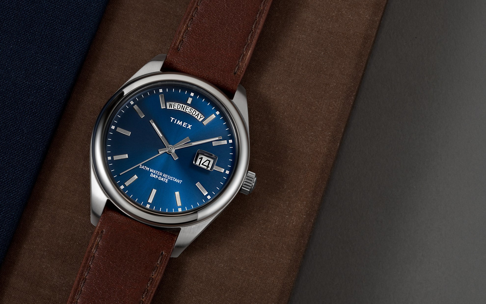 Timex Legacy Quartz Blue Dial Day-Date Leather Band Watch TW2W57200 with brown strap on stylish background.