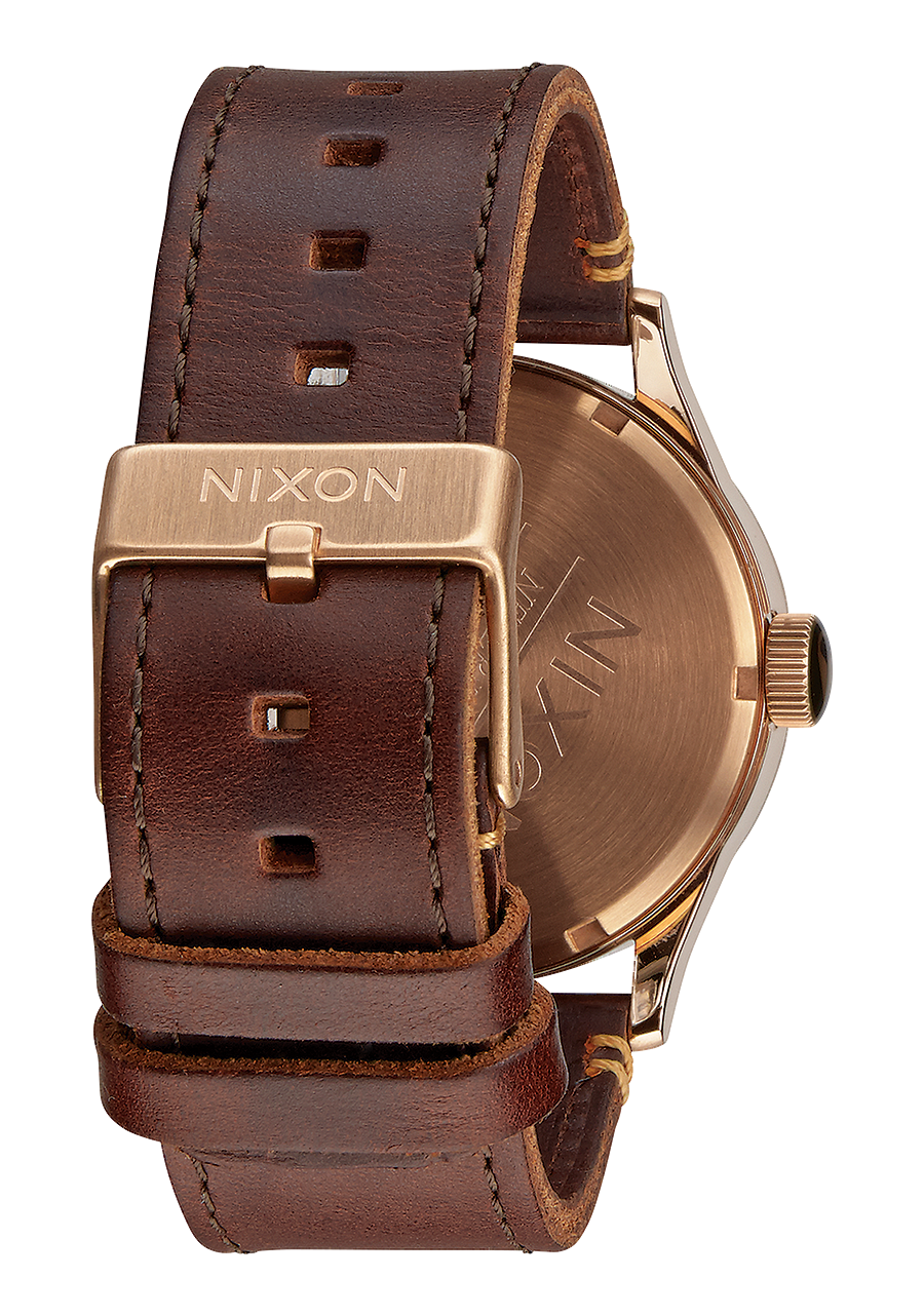 Wristwatch with a brown leather strap and gold-toned case bearing the Nixon brand name.