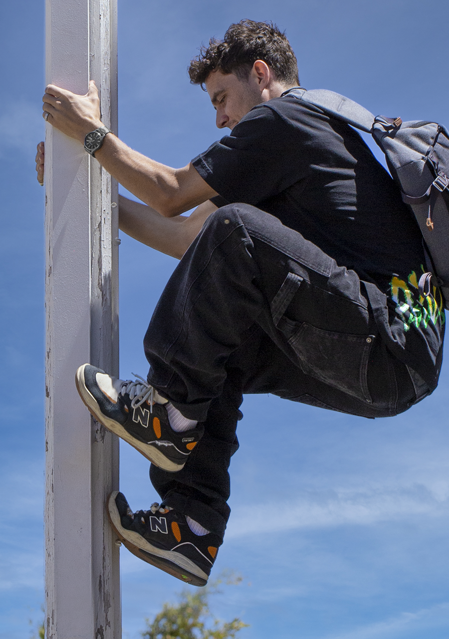 Person climbing a metal pole or structure while wearing a backpack.