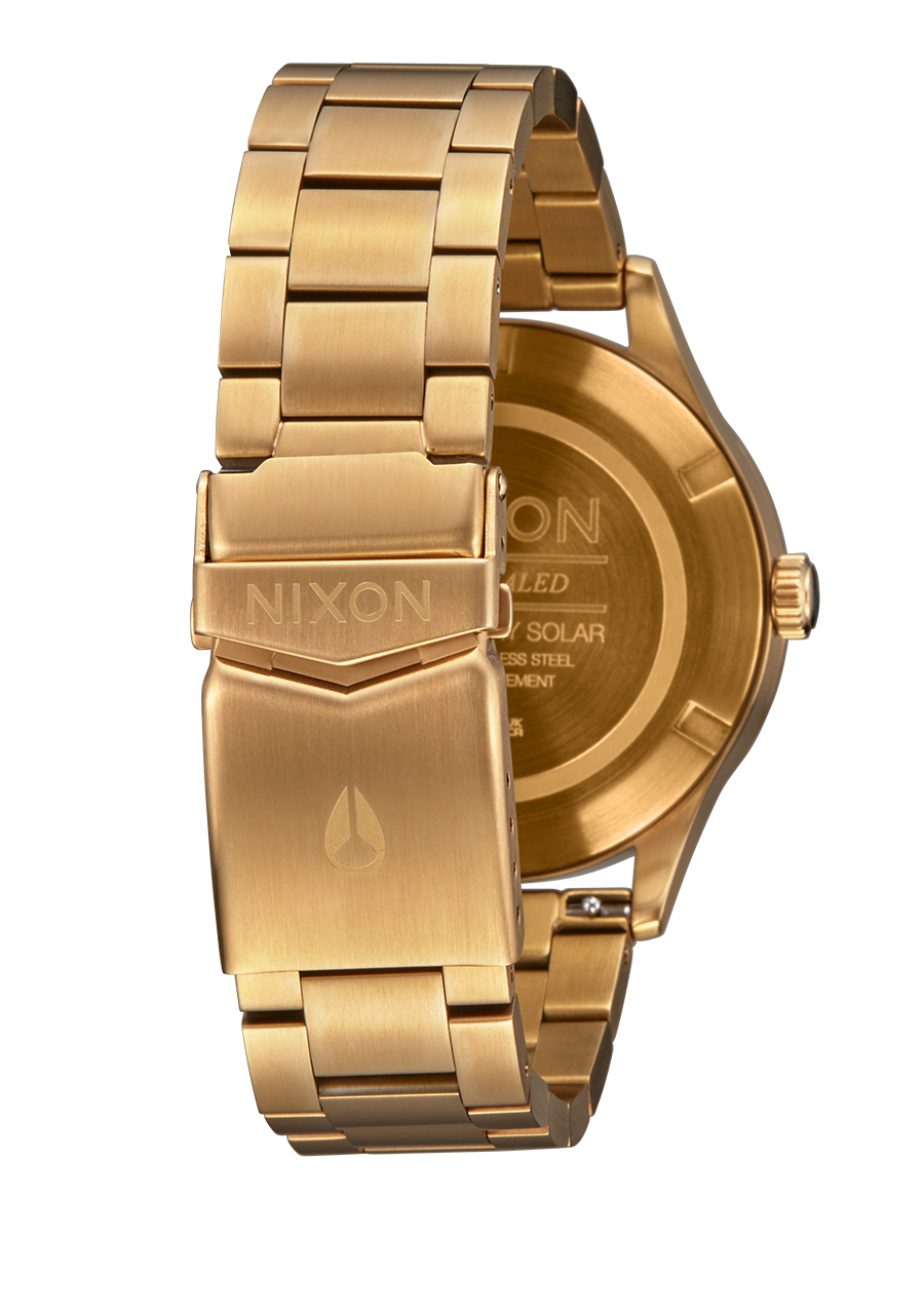 Gold-toned wristwatch with a metal bracelet and Nixon branding on the clasp and case back.