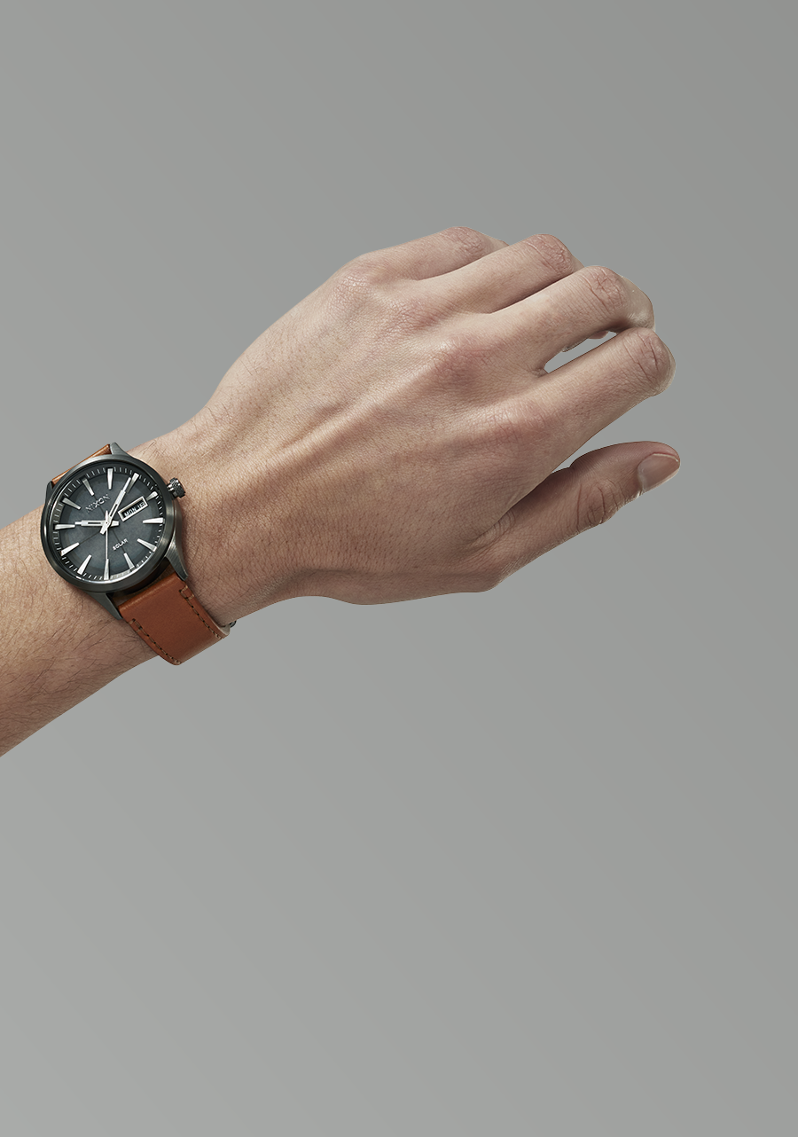 Wristwatch with a black face and brown leather strap worn on a person’s wrist.