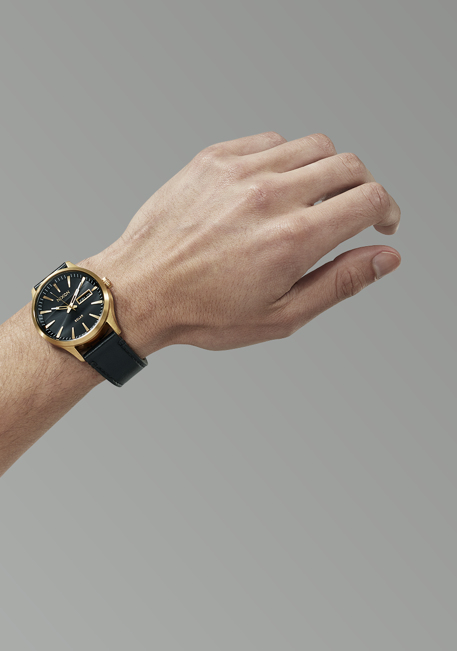 Wristwatch with a black face and gold-toned case on a person’s wrist.