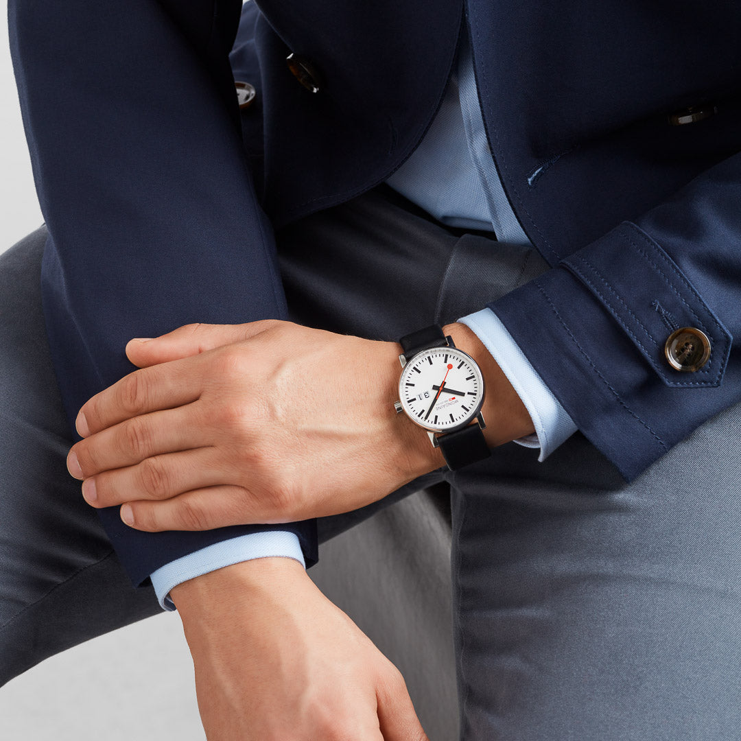 Wristwatch with a white face and black leather strap worn on a person’s wrist.