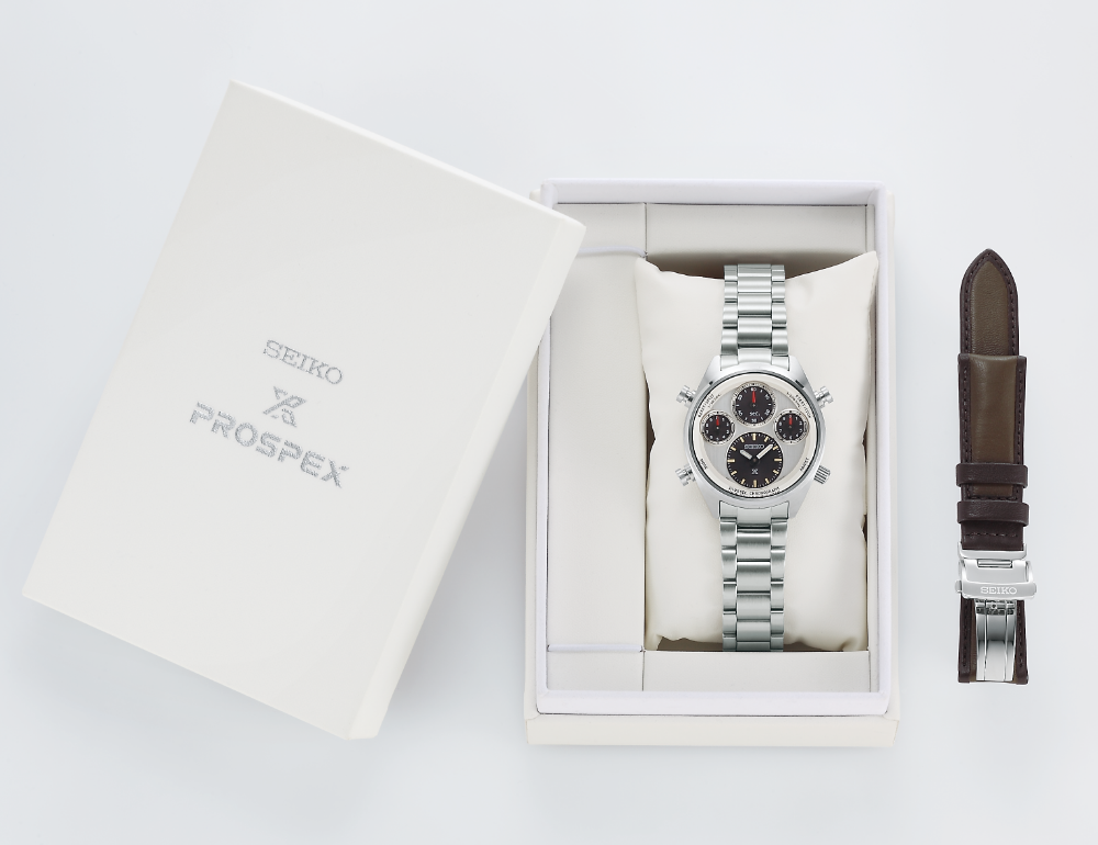 Luxury wristwatch with a silver metal band and multiple dials, presented in a white box alongside an additional leather strap.