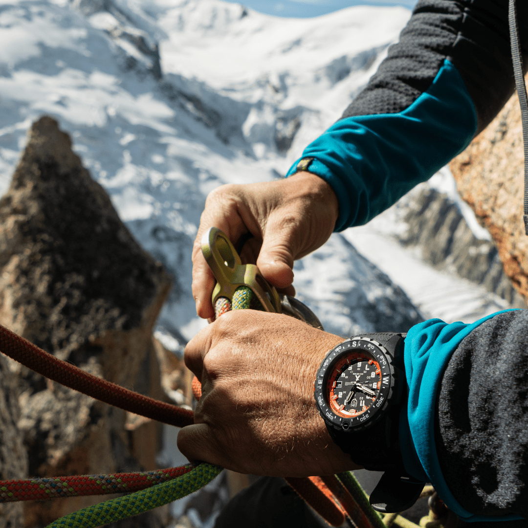 Wristwatch with a black face and orange accents worn by someone handling climbing equipment.