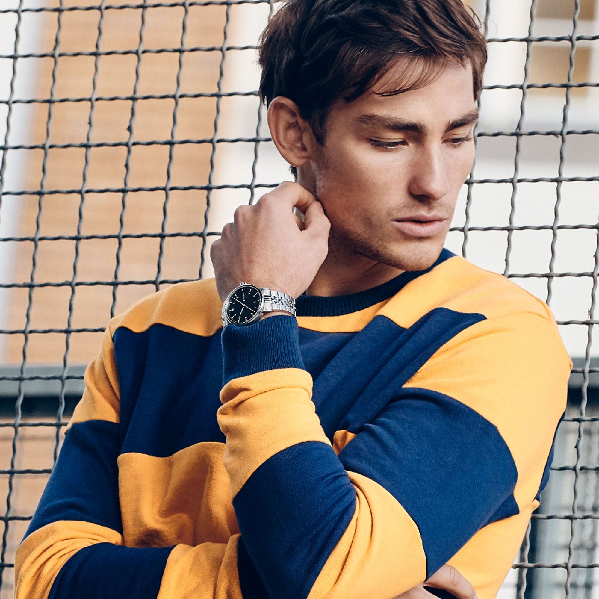 Young man wearing a blue and yellow striped sweater and a wristwatch.