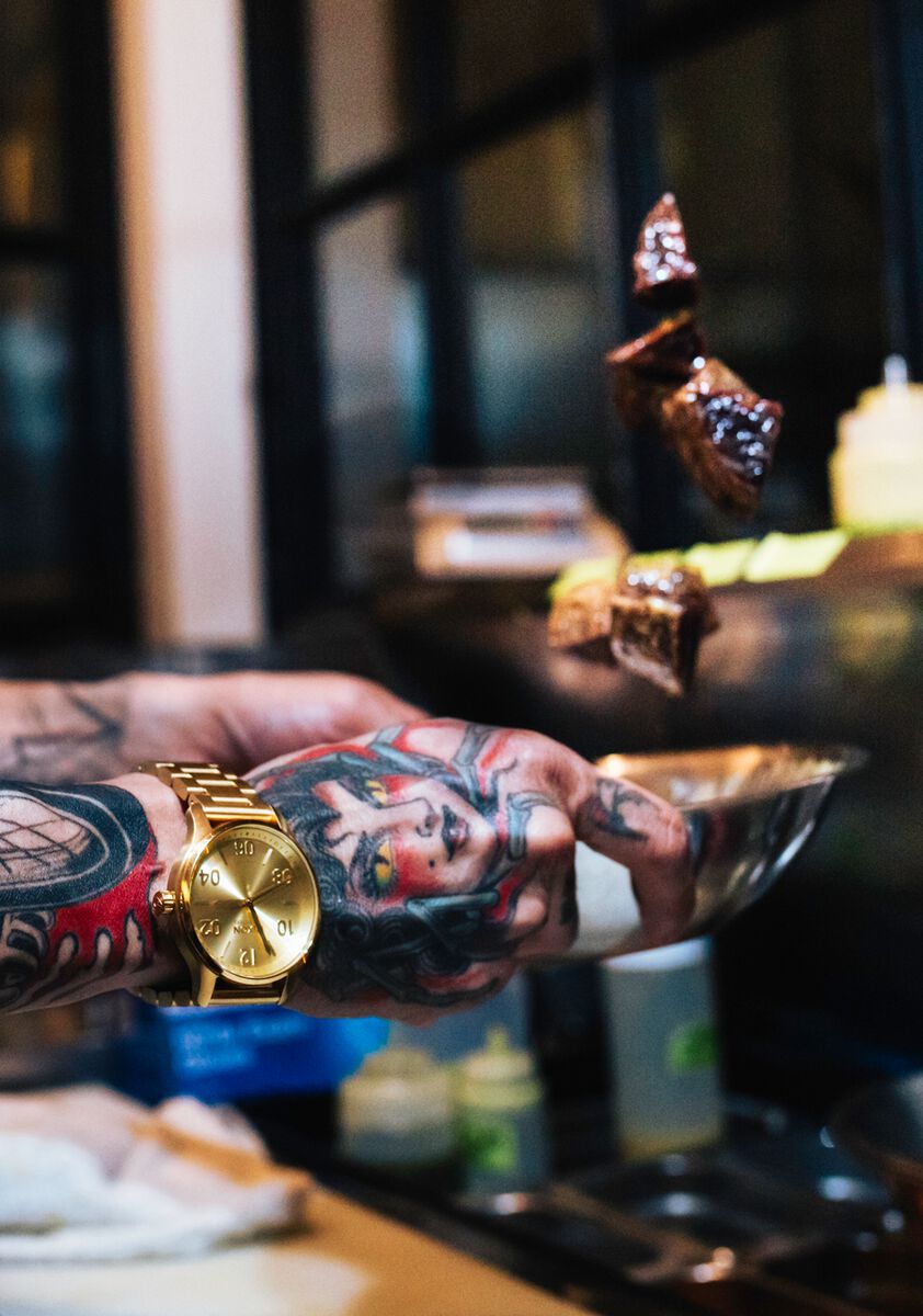 Tattooed arm wearing a gold watch.