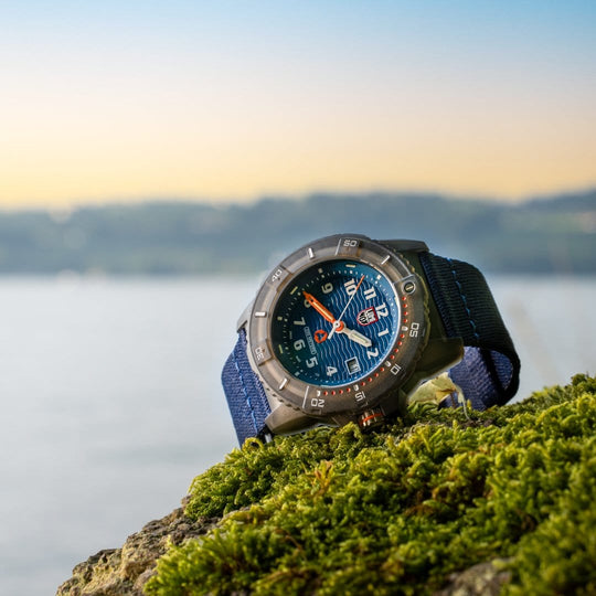 Rugged sports watch with a blue face and fabric strap resting on moss.