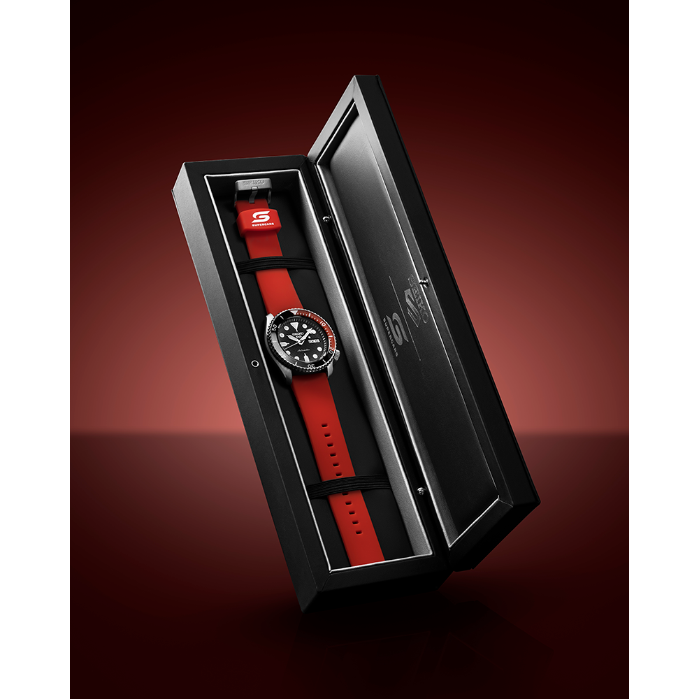 Luxury wristwatch with a black face and red strap displayed in an open presentation box.