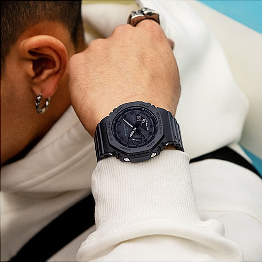 Black wristwatch with a round face and digital display worn on someone’s wrist.