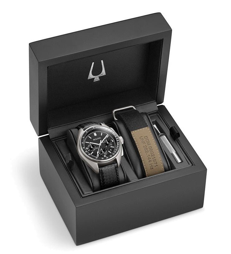 Luxury wristwatch with a black dial in an open presentation box alongside additional accessories.