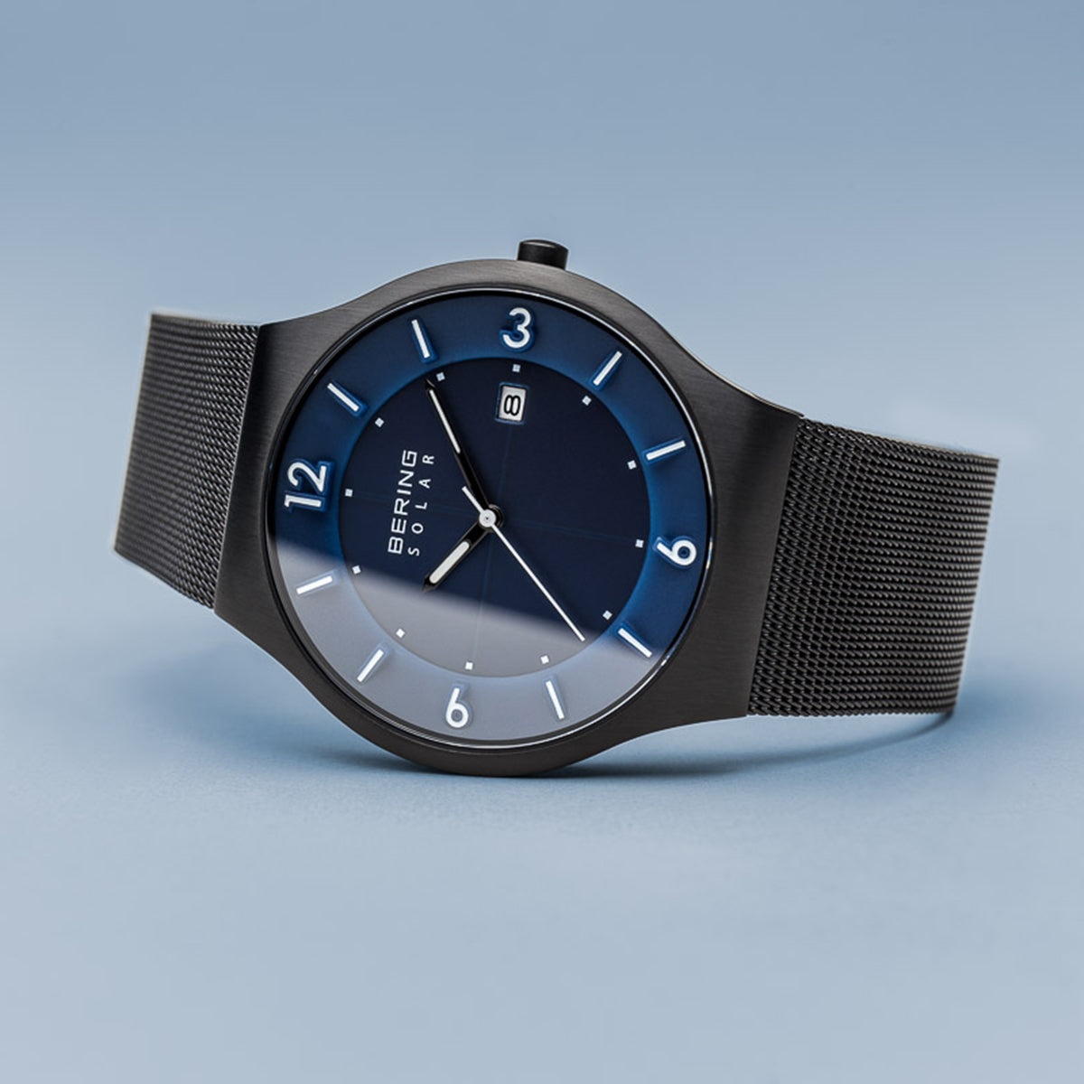 Sleek wristwatch with a dark mesh band and blue-gray gradient dial.