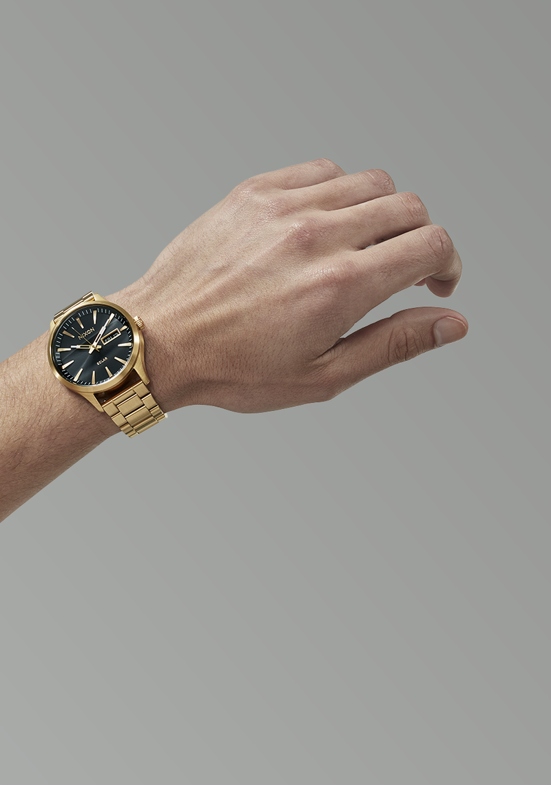 Gold wristwatch with a black dial worn on a person’s wrist.