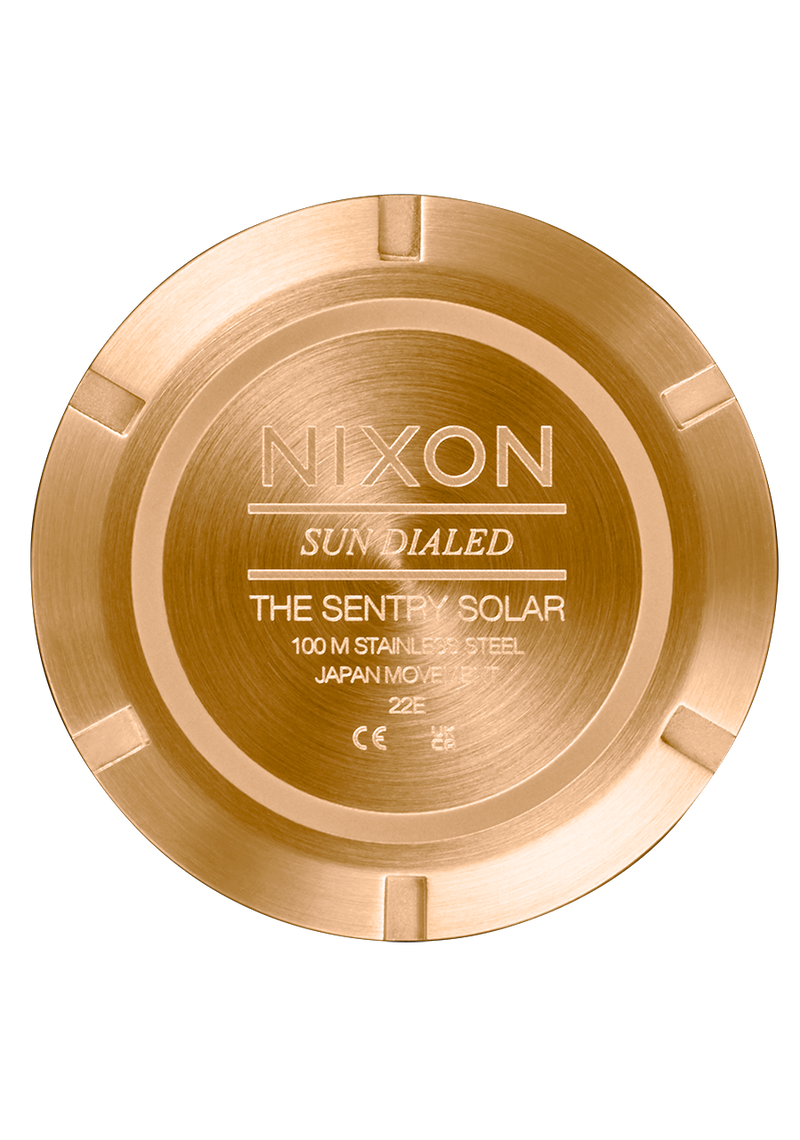 Gold-colored circular watch case back with ’Nixon’ branding and product details engraved.