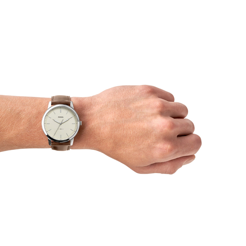 Wristwatch with a brown leather strap and white dial on a person’s wrist.