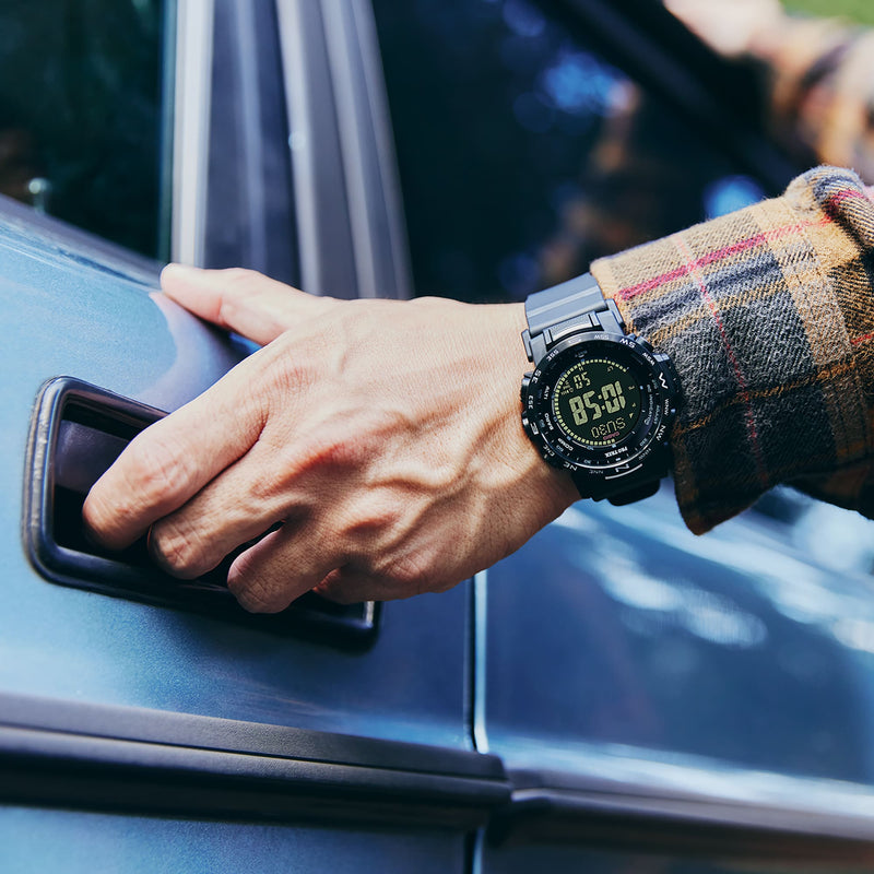 Digital sports watch with a black face worn on a wrist reaching for a car door handle.