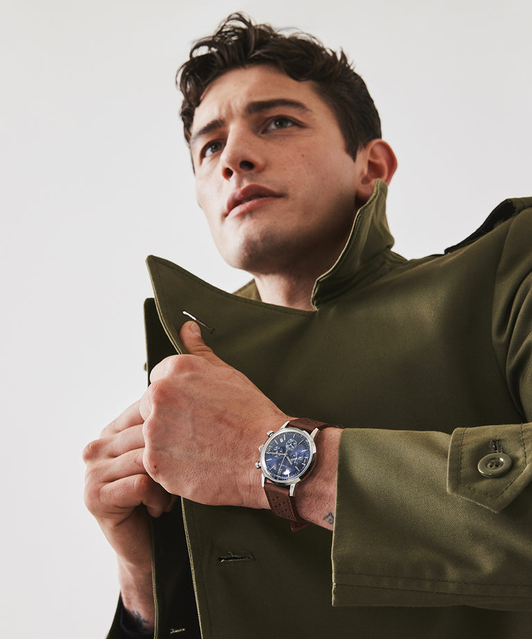 Wristwatch with a blue dial worn by a person in a green jacket.