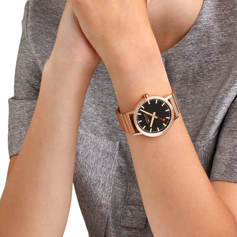 Gold-toned wristwatch with a black dial and mesh metal band.