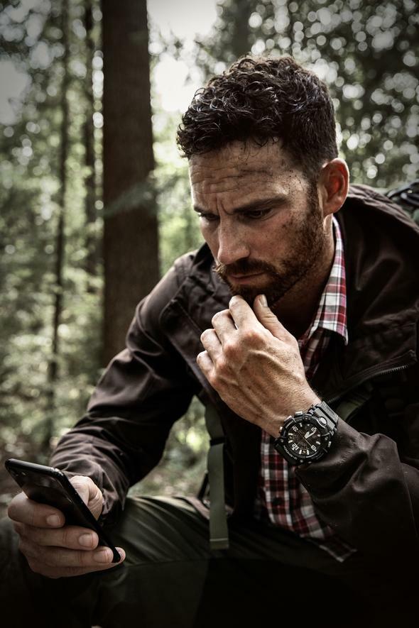 Man with a beard looking at a smartphone while sitting outdoors.