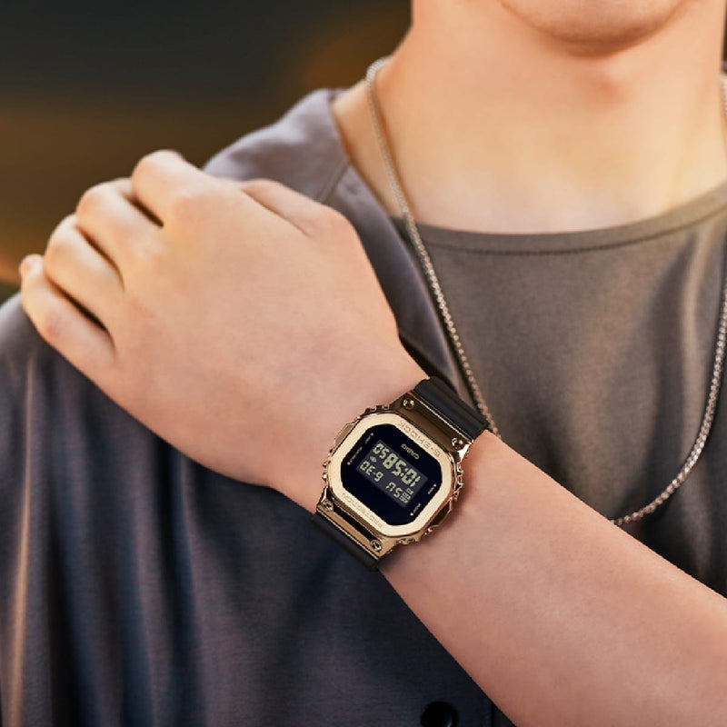 Digital wristwatch with a square face and gold-colored metal band.