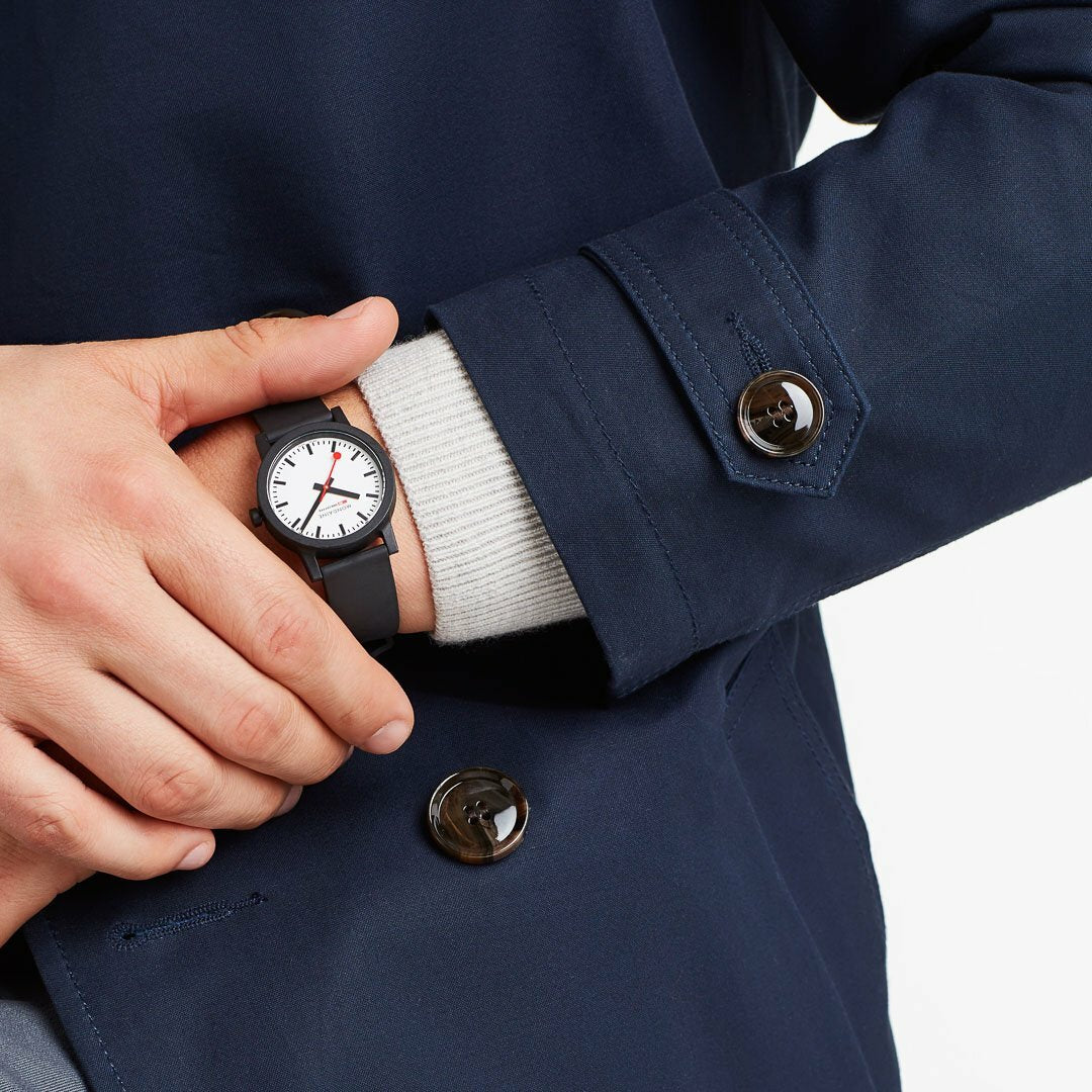 Wristwatch with a white face and black strap visible beneath a navy blue coat sleeve.