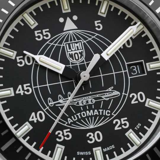 Close-up of a black-faced wristwatch dial with luminous markings and a globe design.