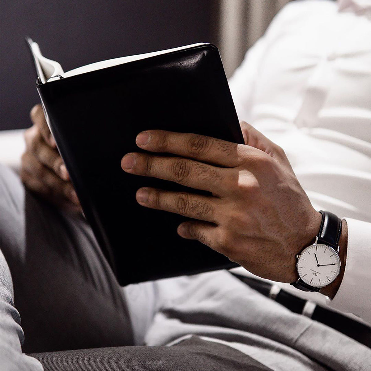 Black book or journal being held open by hands wearing a wristwatch.